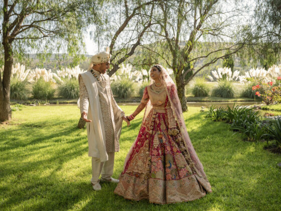 Neha y Sahil tomados de la mano con atuendos nupciales indios en los jardines de Rancho Luna Escondida, San Miguel de Allende