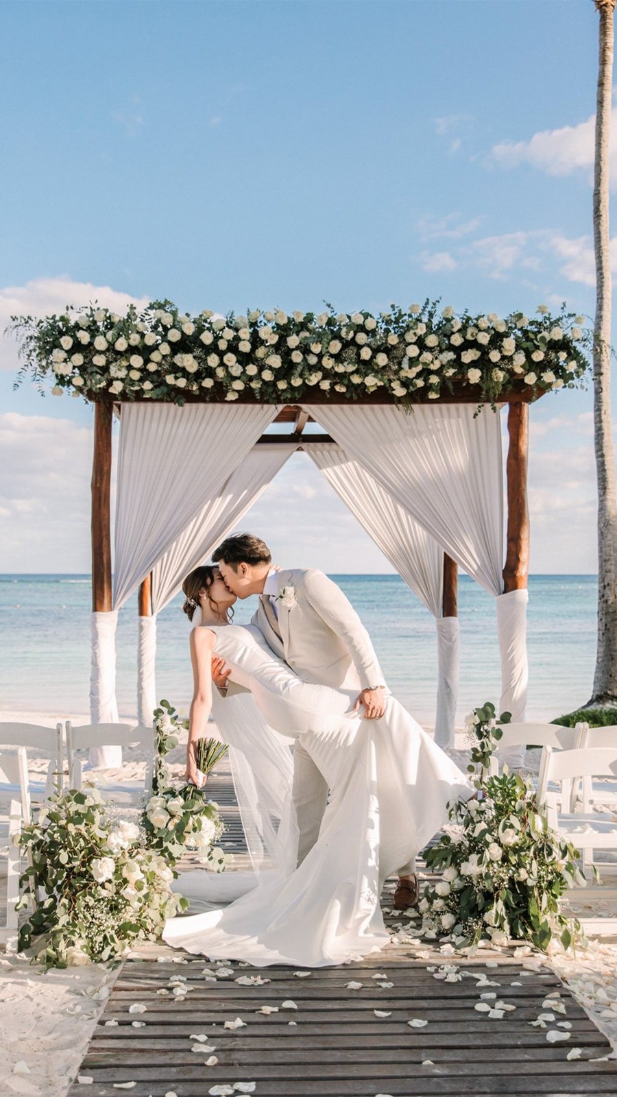 Novios se besan bajo un arco floral frente al mar en una boda destino en la playa