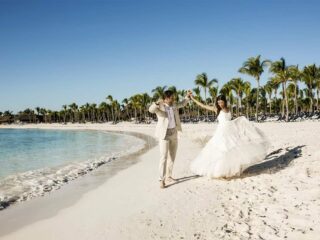 Pareja de novios caminando por una playa de arena blanca con palmeras en el Caribe mexicano