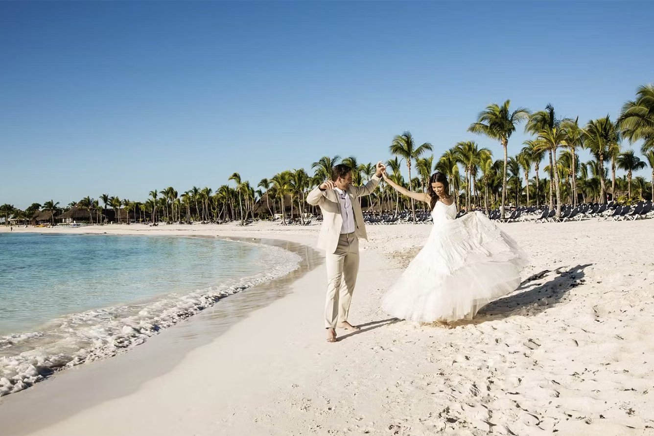 Pareja de novios caminando por una playa de arena blanca con palmeras en el Caribe mexicano
