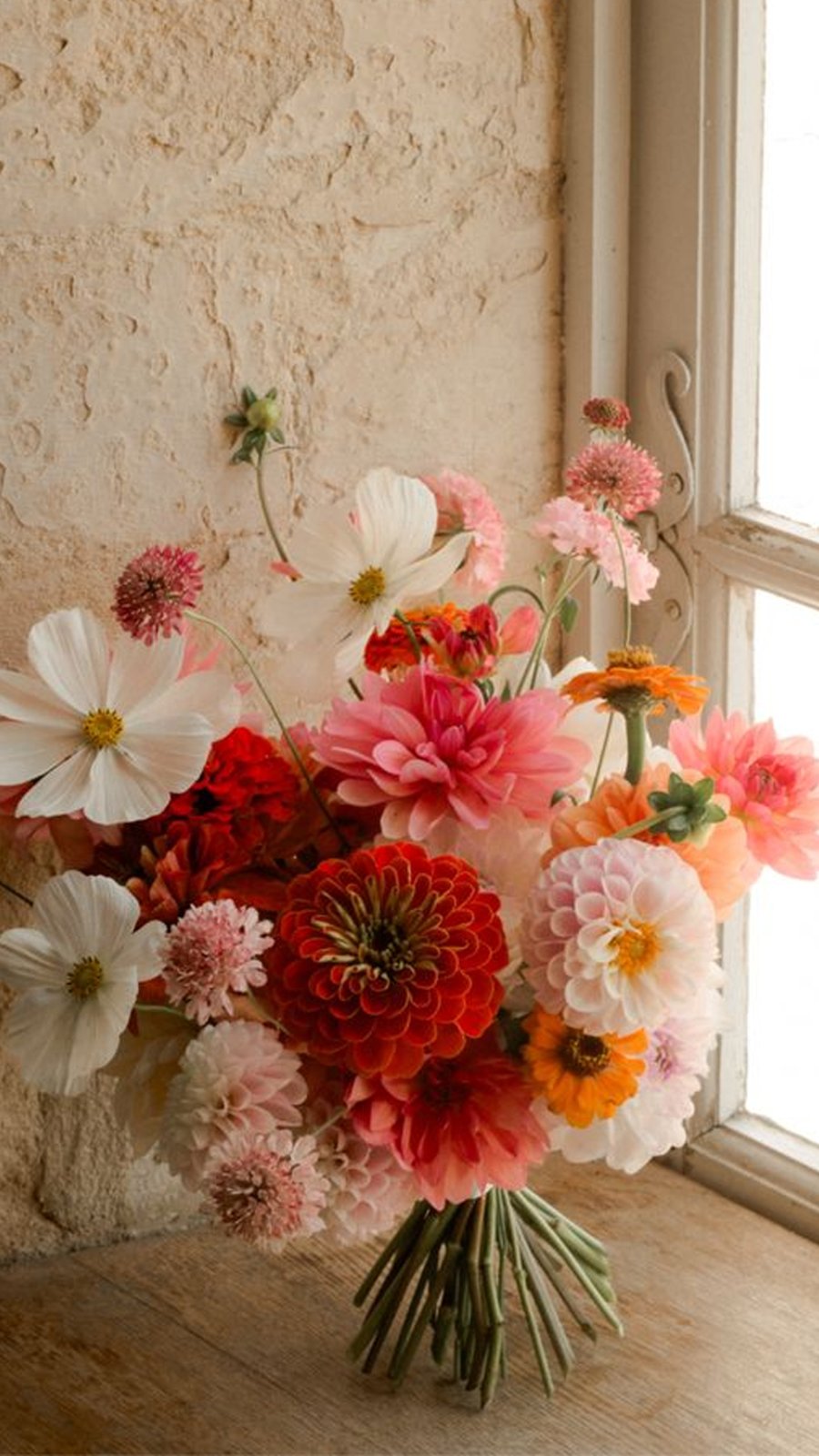 Ramo de flores en tonos coral, rosa y blanco junto a una ventana