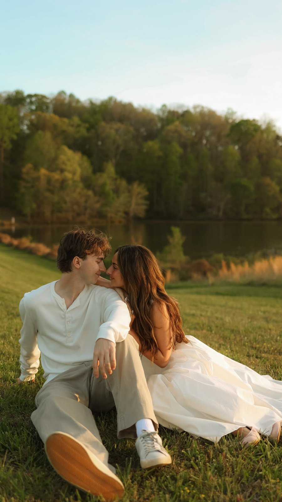Pareja sentada en el pasto junto a un lago al atardecer
