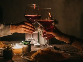 Pareja brinda con copas de vino tinto en una cena a la luz de las velas