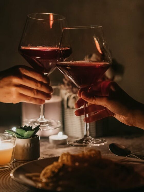 Pareja brinda con copas de vino tinto en una cena a la luz de las velas