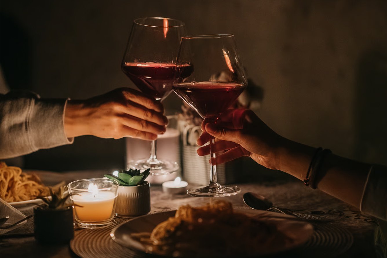 Pareja brinda con copas de vino tinto en una cena a la luz de las velas