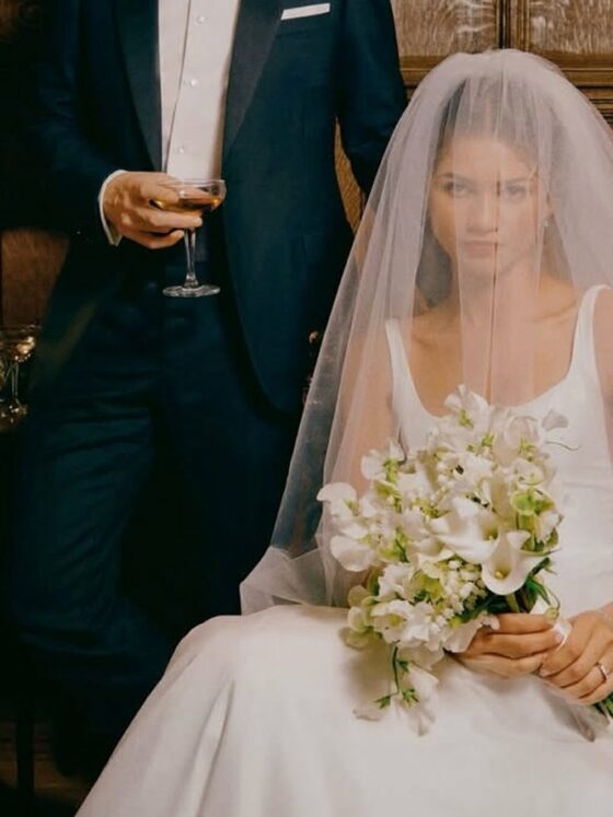 Novia con velo largo y ramo de flores blancas sentada en un salón con paneles de madera