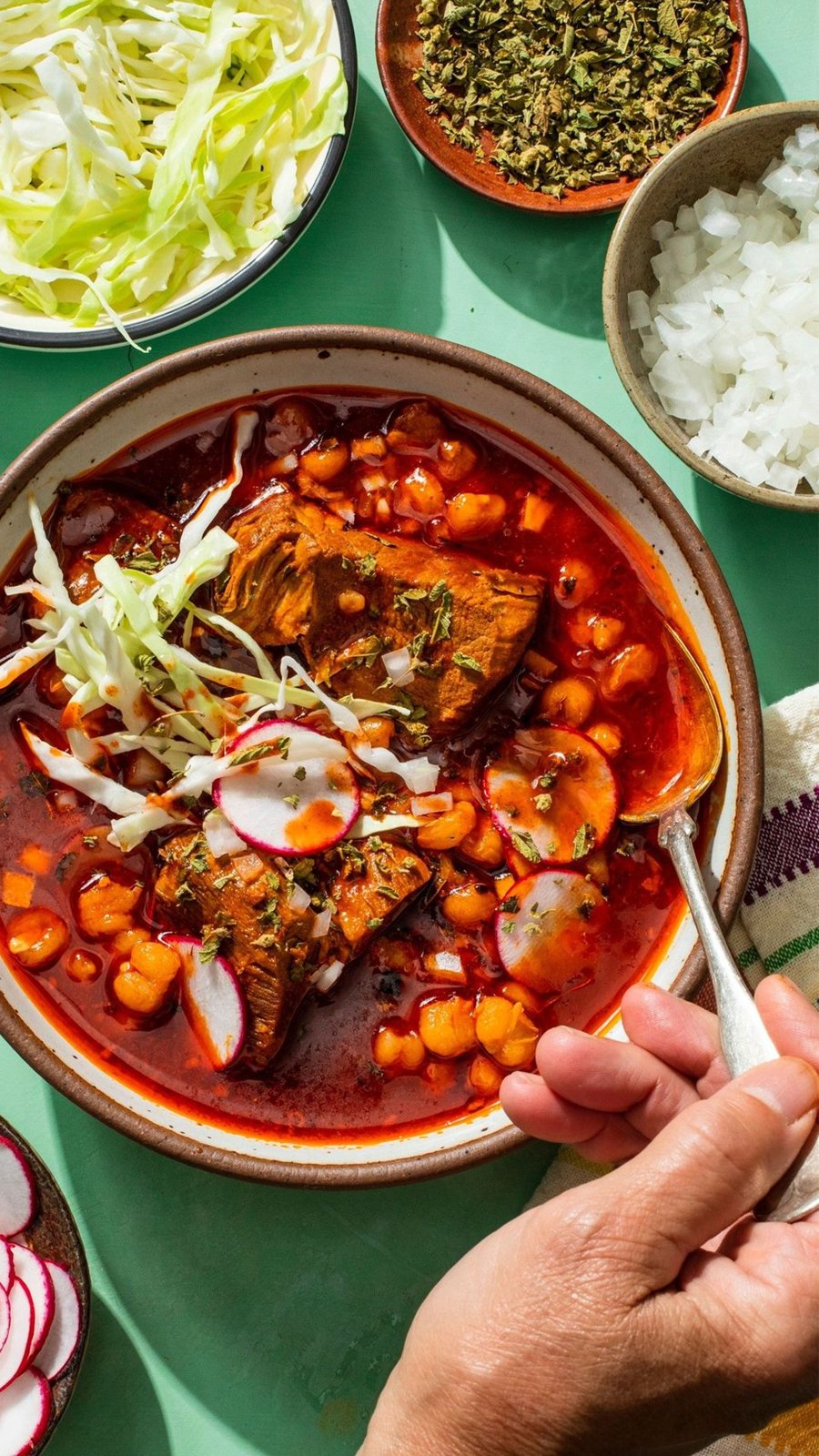 Plato de pozole rojo con lechuga, rábano, orégano y cebolla