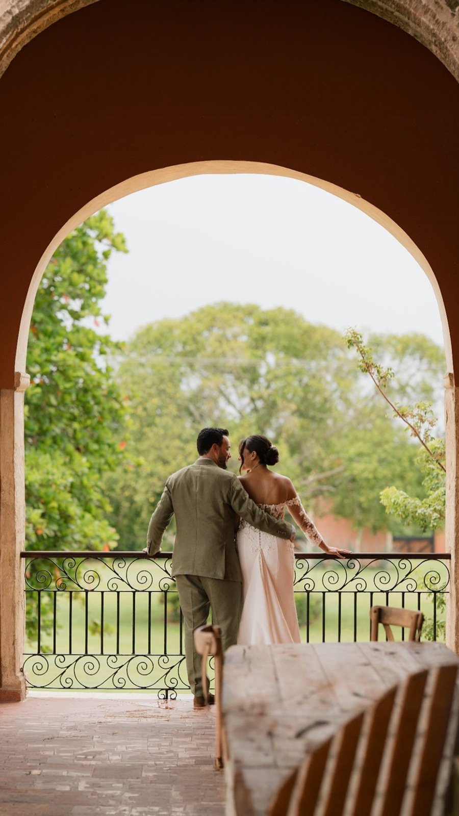 Novios contemplan el jardín desde el balcón arqueado de una hacienda