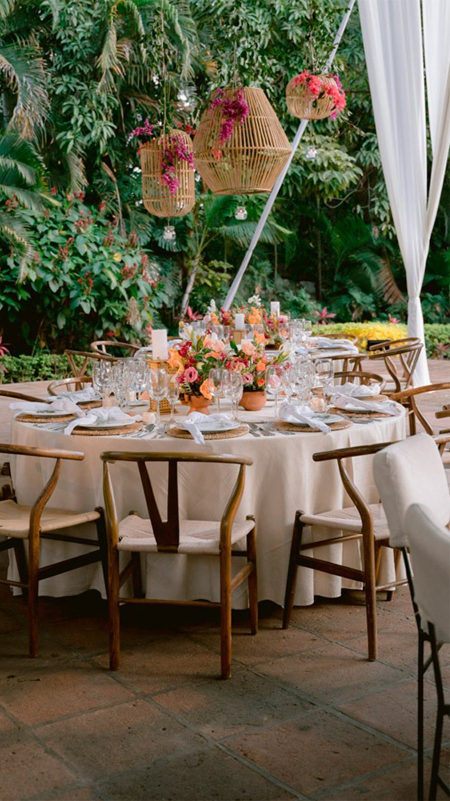 Mesa redonda con flores y lámparas de mimbre en el jardín tropical de una hacienda