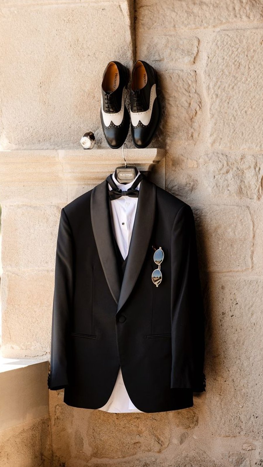Esmoquin negro colgado junto a zapatos bicolor listos para el día de la boda