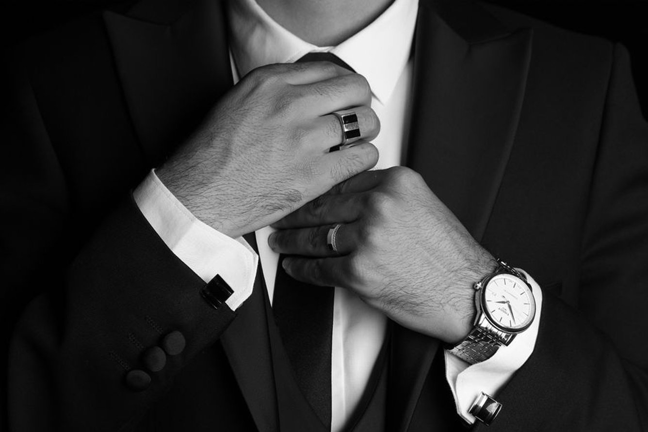 Novio se ajusta la corbata con reloj y anillo en primer plano, en blanco y negro