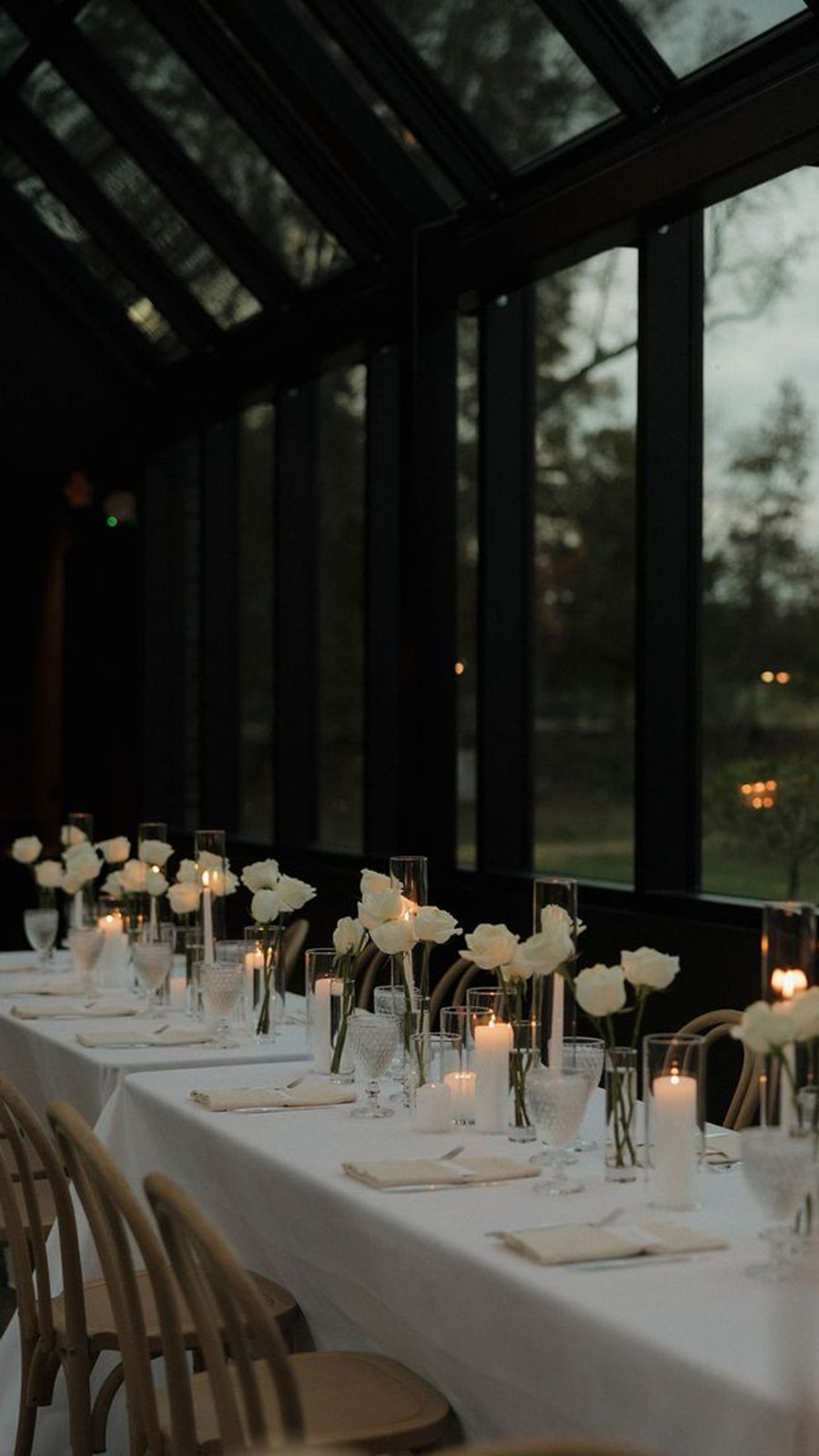 Mesa minimalista con mantel blanco, velas y flores blancas en un invernadero