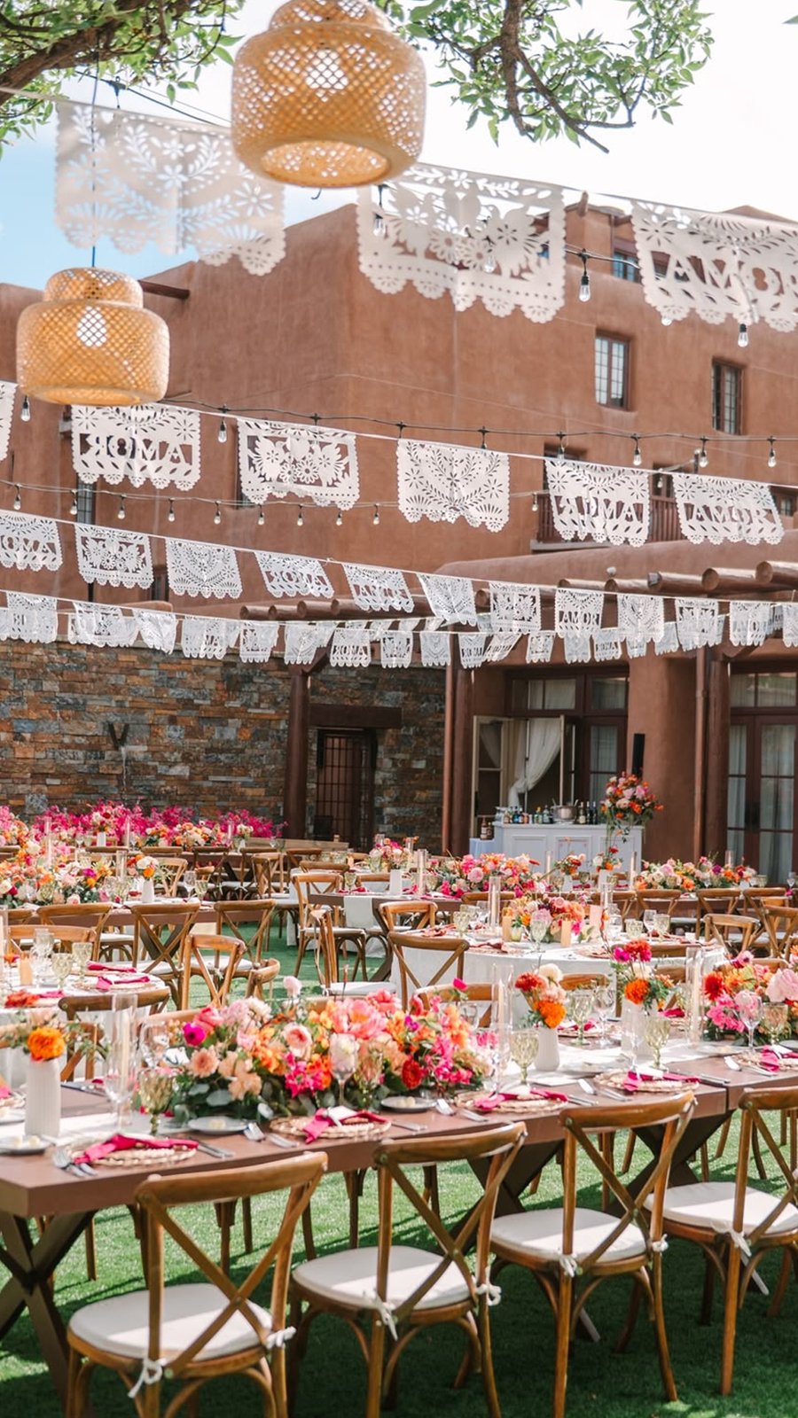 Banquete con papel picado, flores de colores y sillas de madera en un patio