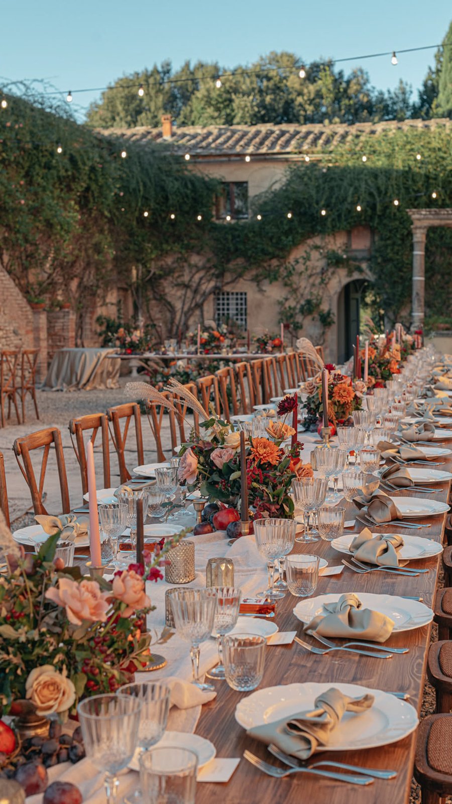 Mesa larga con flores en tonos naranja bajo luces colgantes en una villa estilo toscano