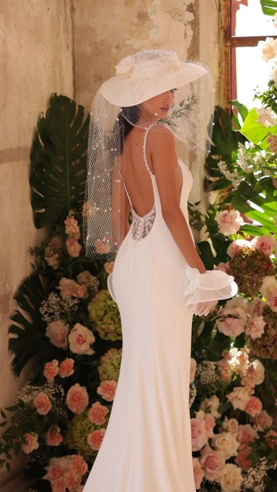 Novia con sombrero de ala ancha y velo, vestido de espalda descubierta