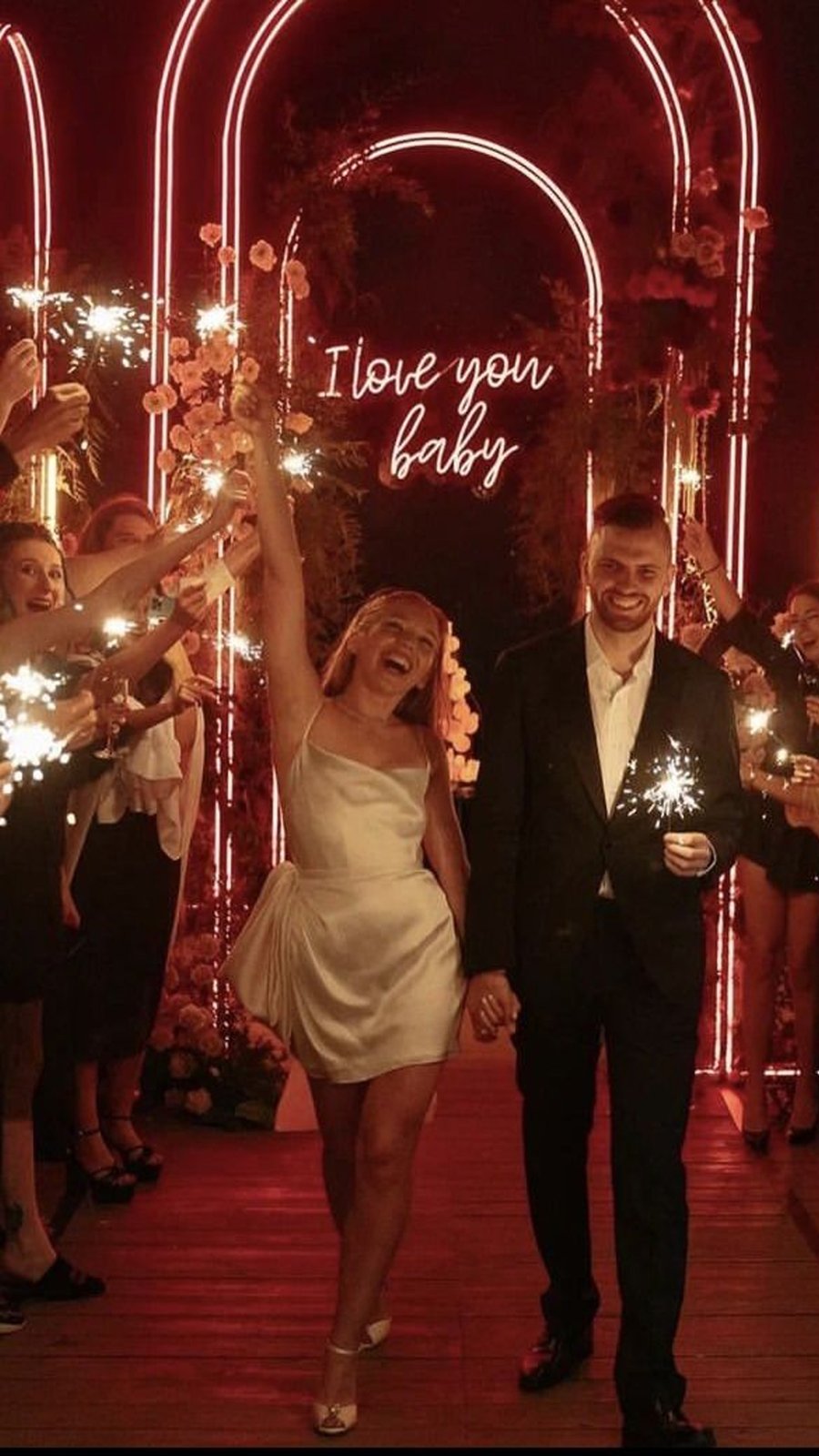 Novios salen entre bengalas bajo un letrero de neón I love you baby