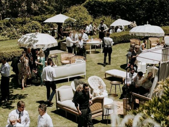 Invitados conviven en un jardín con salas lounge y sombrillas durante una tornaboda