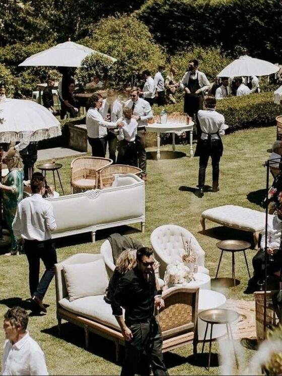 Invitados conviven en un jardín con salas lounge y sombrillas durante una tornaboda