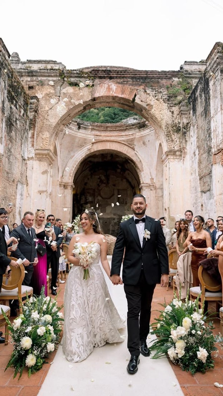 Novios caminan entre sus invitados al salir de la ceremonia en las ruinas de una iglesia
