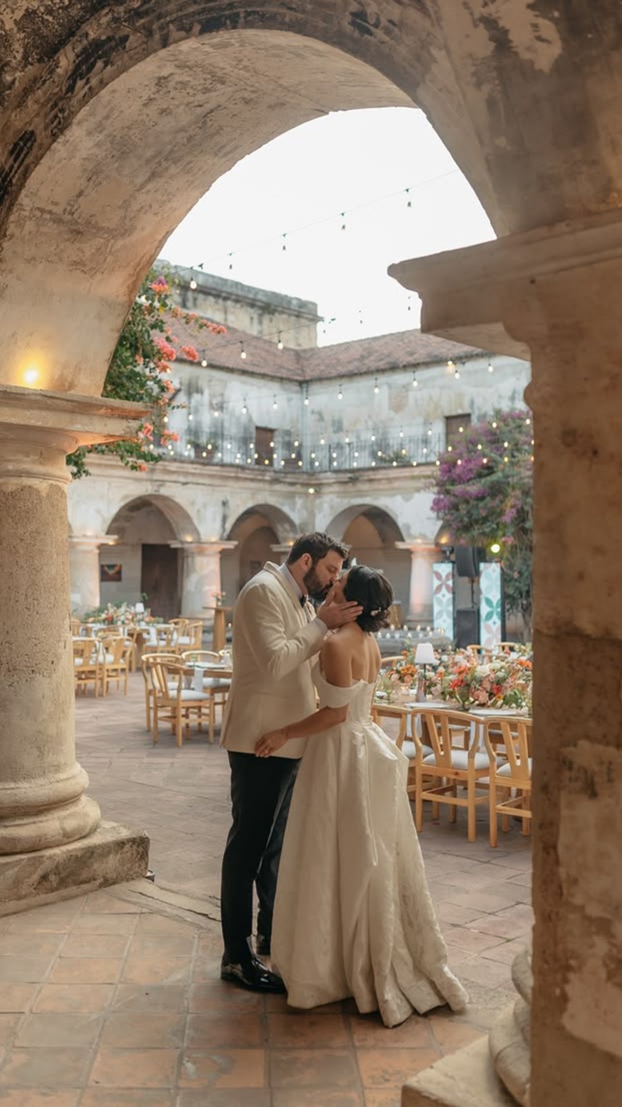 Novios se besan bajo una arcada en el patio de un hotel colonial preparado para la recepción