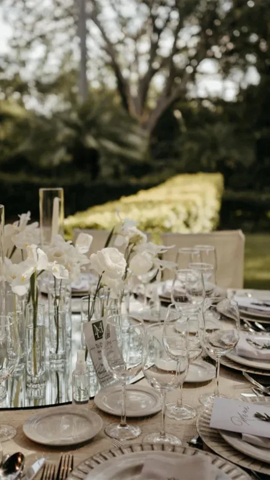 Mesa con cristalería y centros de orquídeas blancas en un jardín