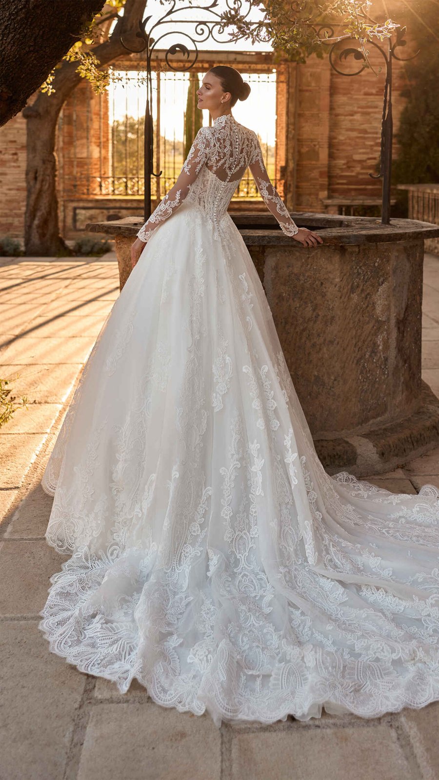 Vestido de novia de encaje con cauda larga visto de espaldas en un patio