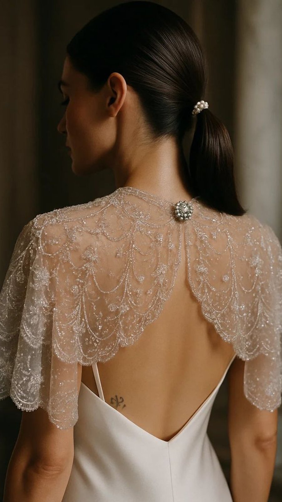 Capa corta de encaje con pedrería sobre un vestido de espalda descubierta