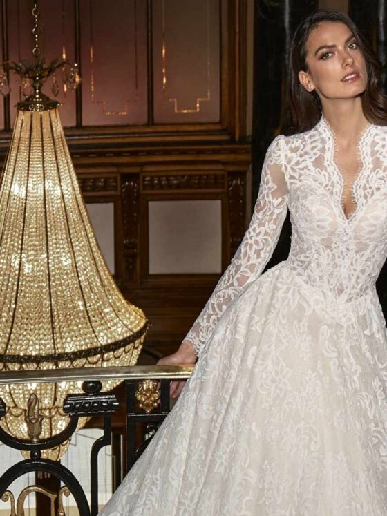 Novia con vestido de encaje de manga larga y escote en V en un salón con candil