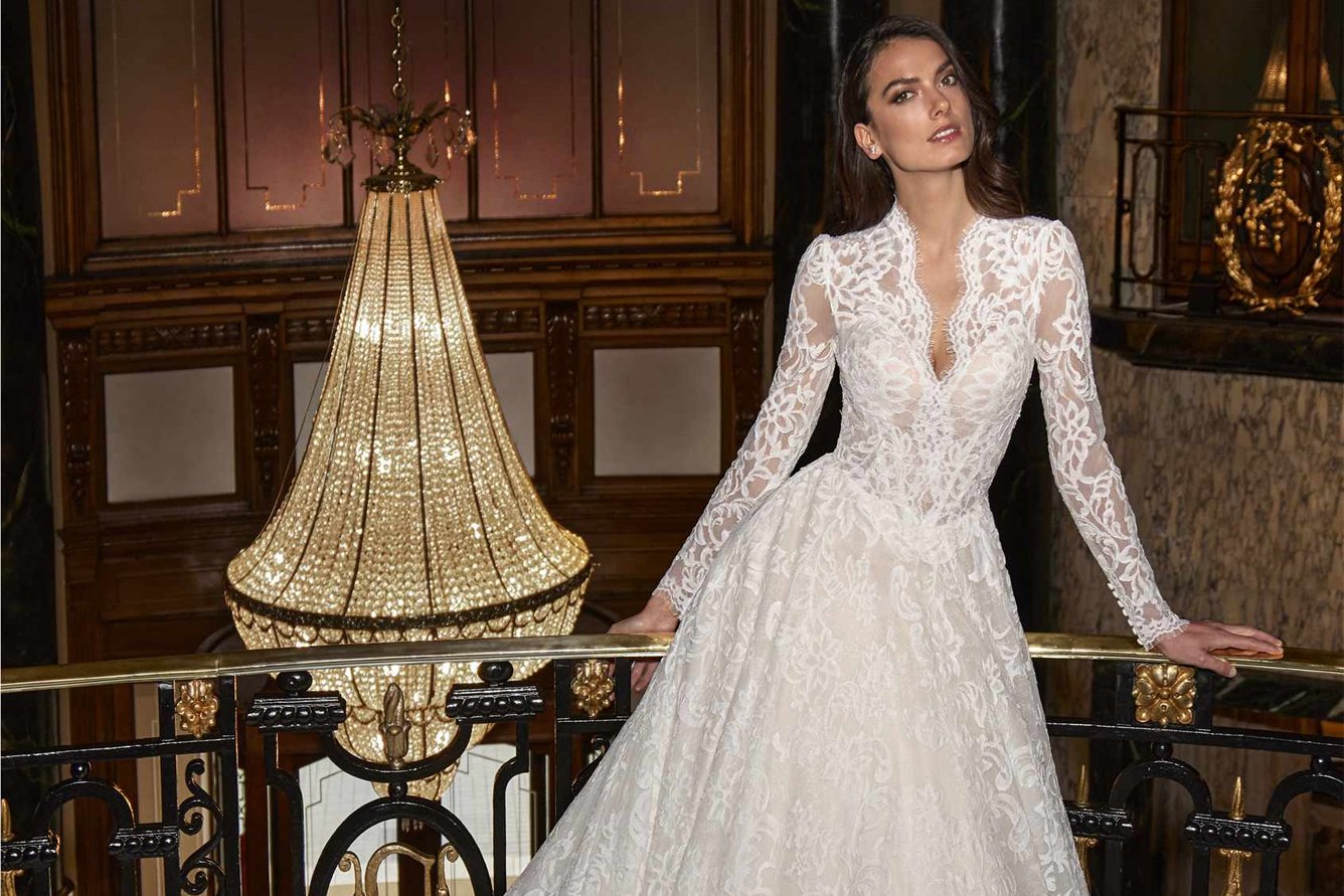 Novia con vestido de encaje de manga larga y escote en V en un salón con candil